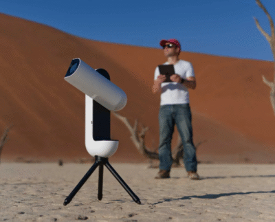 Sleek smart telescope set up under a starry night sky showcasing modern stargazing technology. Person using a smart telescope connected to a smartphone app for effortless stargazing. Compact high-tech telescope offering $300 discount displayed on a rooftop under the Milky Way. Family enjoying a stargazing session using an AI-powered telescope with automated tracking. Close-up of a smart telescope lens capturing clear images of distant stars and planets. Futuristic telescope interface on a smartphone controlling focus and tracking. Digital illustration comparing traditional telescopes with next-generation smart designs.