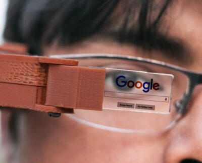 Person wearing AI smart glasses capable of instant facial recognition. AI glasses scanning surroundings and identifying faces in real time. Close-up of smart glasses showing advanced image recognition technology. Digital privacy concerns rising with AI-powered wearable devices. AI glasses capturing and analyzing data in public spaces. User viewing instant information through smart augmented reality glasses. Concept image of privacy risks linked to facial recognition glasses.